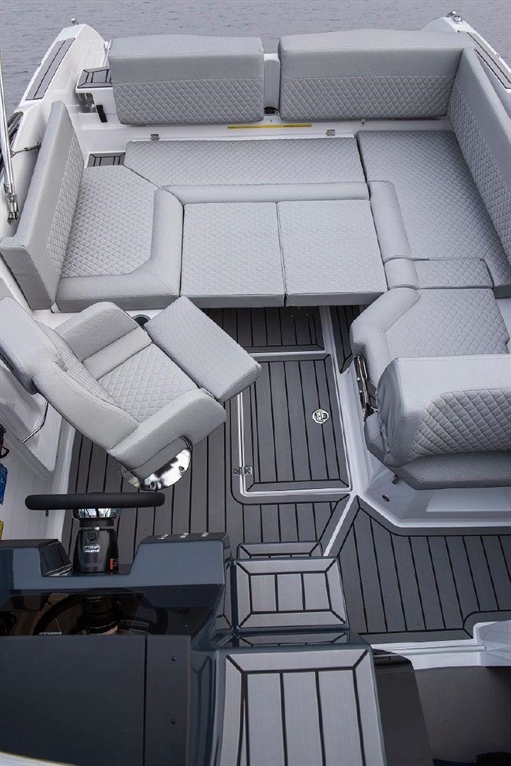Modern boat interior featuring grey cushioned seating and a steering console on a wooden deck.
